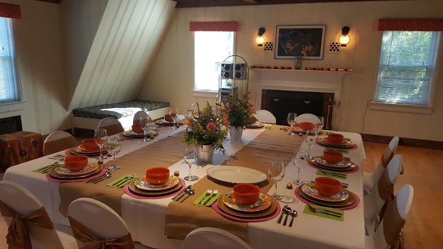 A large table with colorful china and mixed floral centerpieces set for an event of twelve in the Carriage house event space at Morehead Manor