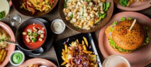 overhead view of a restaurant table with colorful plates including a burger, fries, salad, and soup