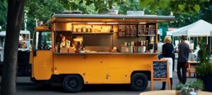 yellow food truck serving customers at an outdoor market with string lights and vendor tents