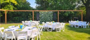 Outdoor wedding reception setup on the lawn at Morehead Manor with round tables, white chairs, a floral backdrop, and string lights.