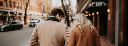 couple walking arm in arm down a charming city street in winter, wearing warm neutral coats
