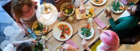 A group of people sits around a table sharing pizza, salad, and drinks during a casual meal.