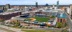 An aerial view of downtown Durham highlights the Durham Bulls baseball stadium surrounded by city buildings and skyline views.